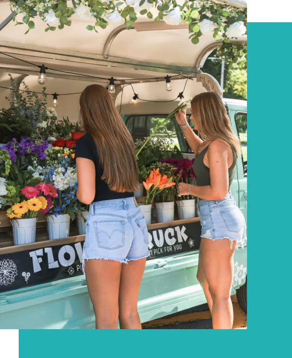 Two women standing in front of a flower truck.